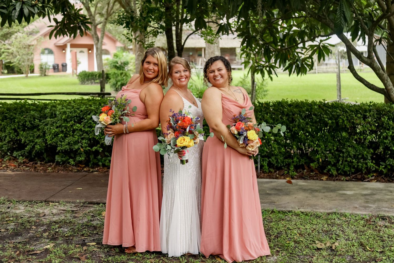 Wedding party poses outdoors in matching pink bridesmaid dresses and white bridal gown with colorful bouquets.