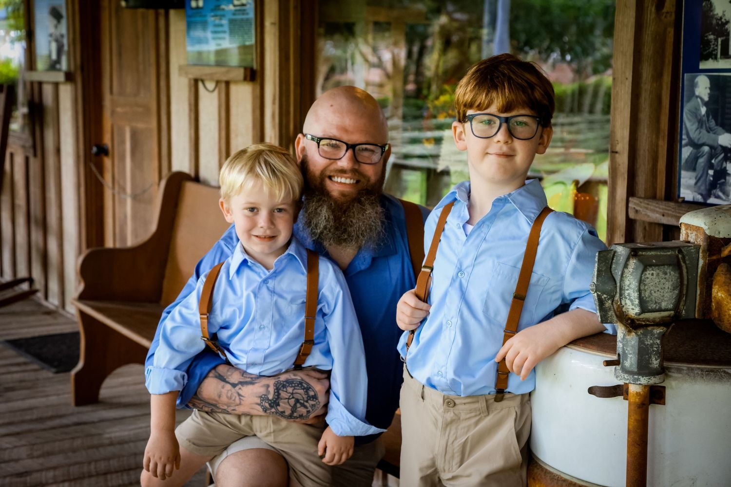 A casual family portrait on a rustic porch with matching blue shirts and suspenders.