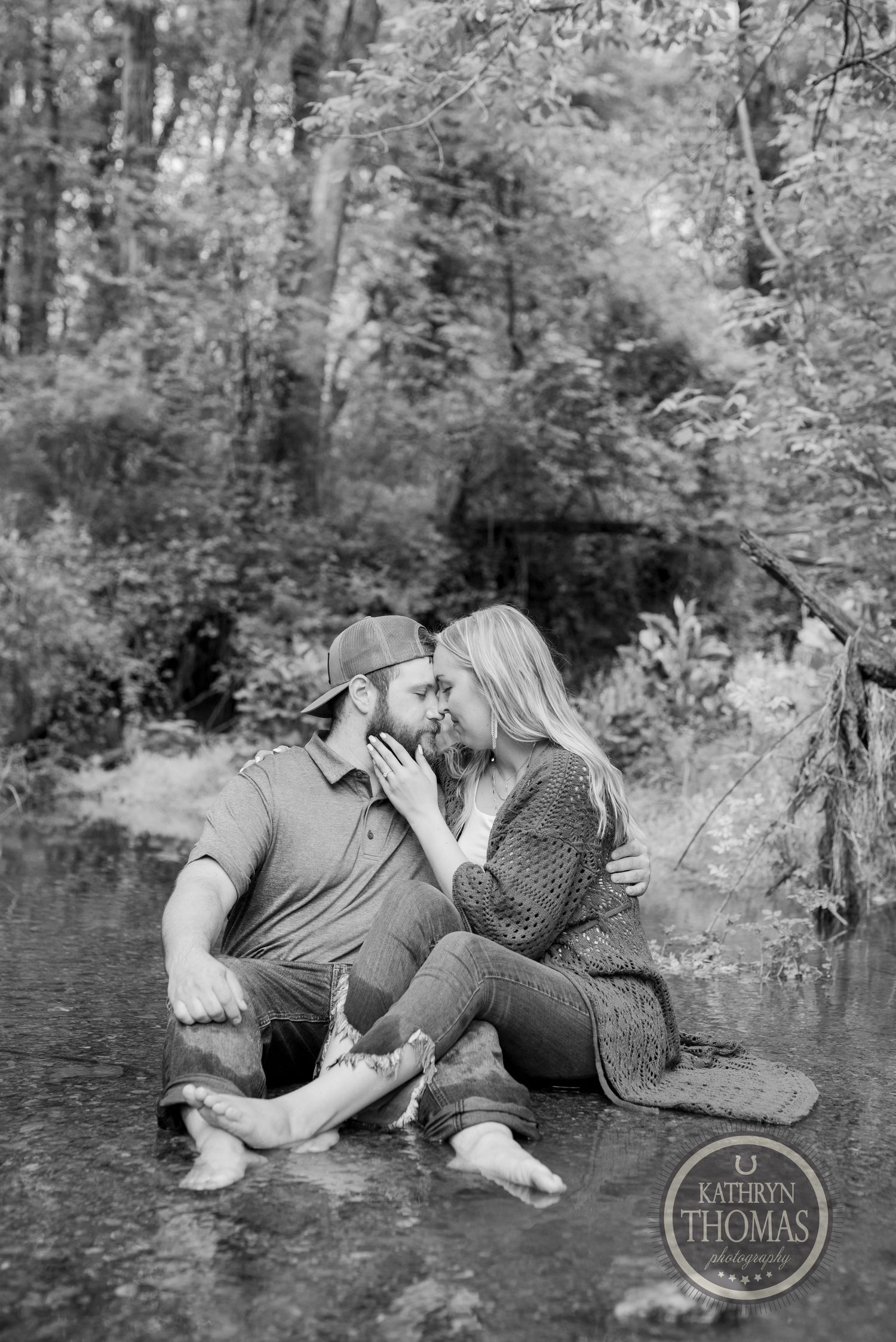 A black and white photo captures an intimate moment between a couple sitting in a creek.