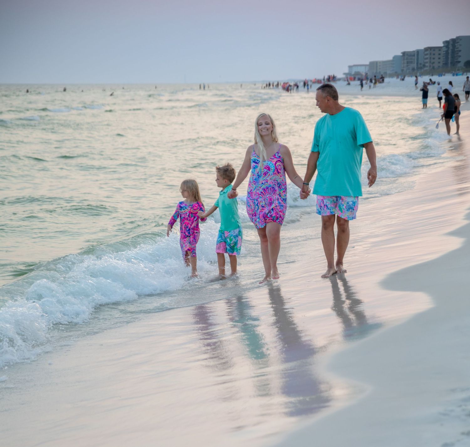 Family holds hands while walking along the shoreline at sunset.