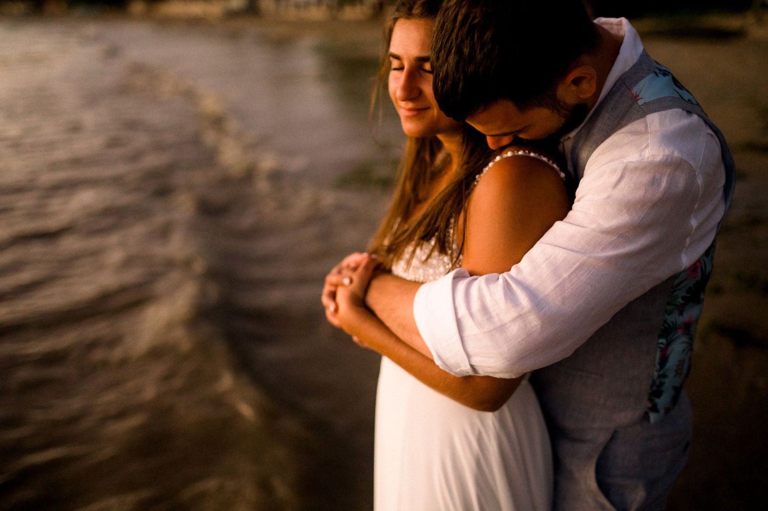 Couple embraces on beach at sunset in romantic moment.