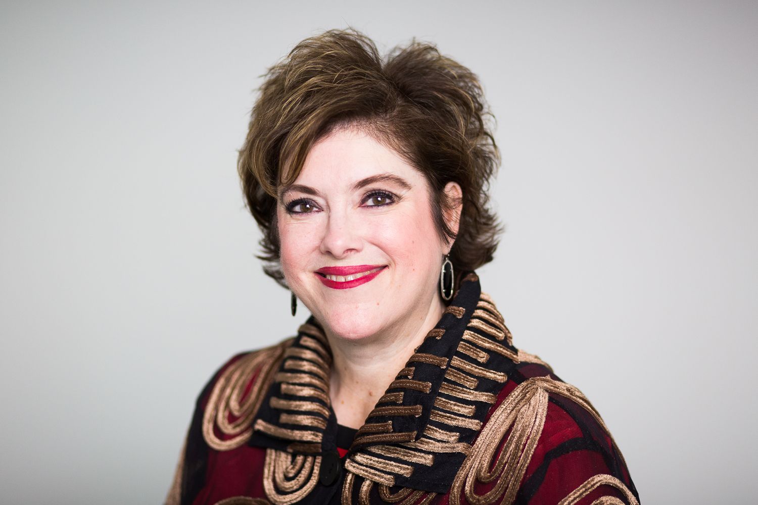 woman facing left with short brown hair red lips jacket with gold piping
