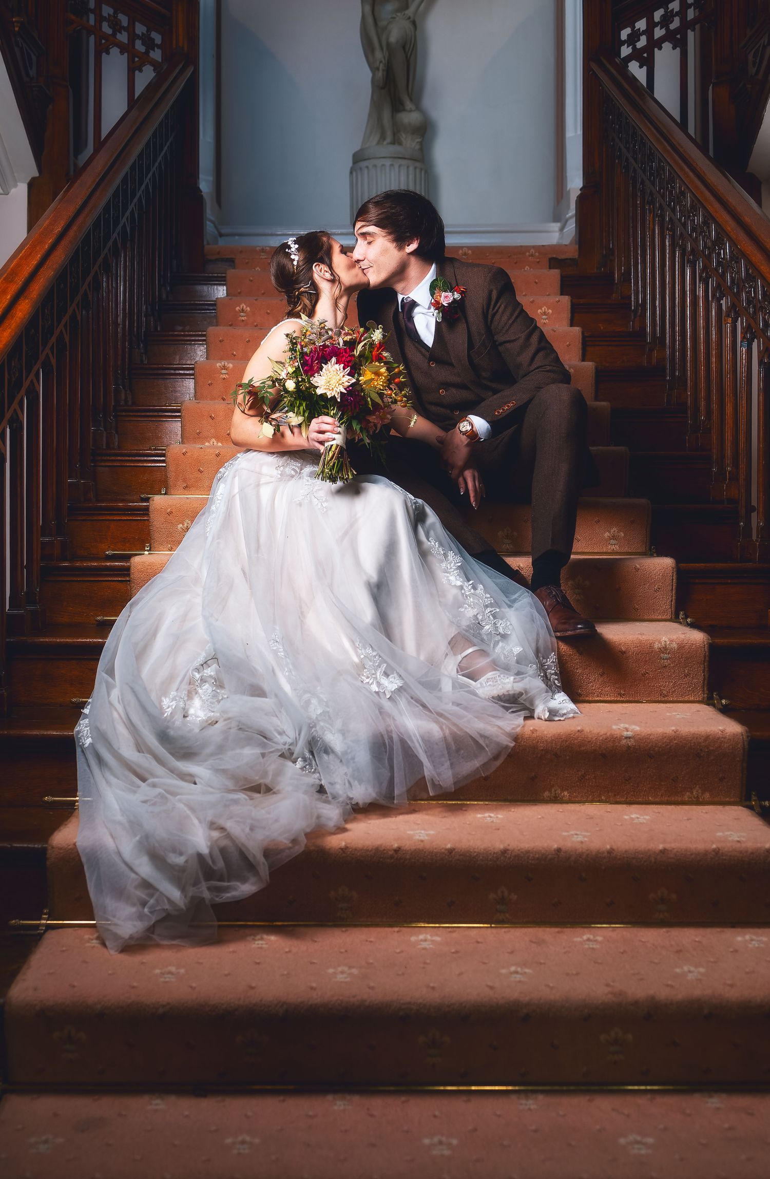 Bride and groom sharing a kiss on a grand staircase with bouquet, romantic wedding photography Southampton