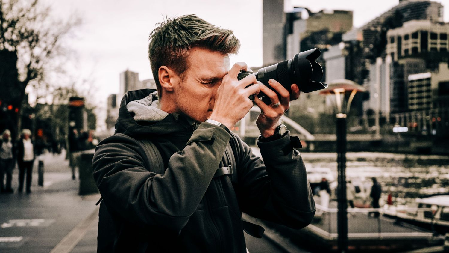 Photographer taking photos on a busy urban street with professional camera equipment.