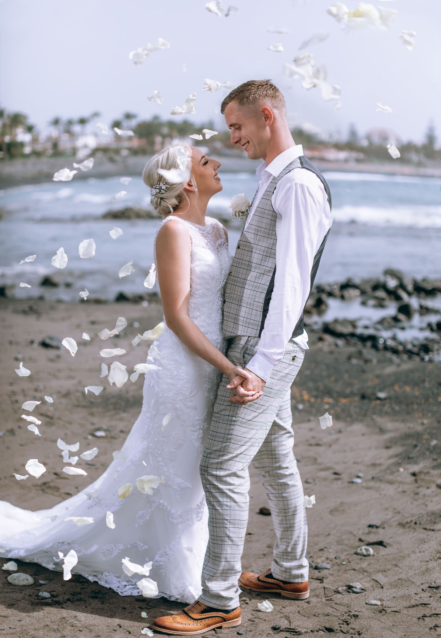 Bride and groom lock eyes lovingly, with rose petals in the air and Tenerife's seaside in the background.