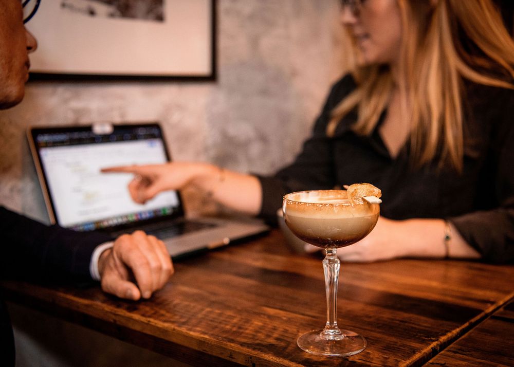 woman pointing to laptop screen with cocktail drink nearby