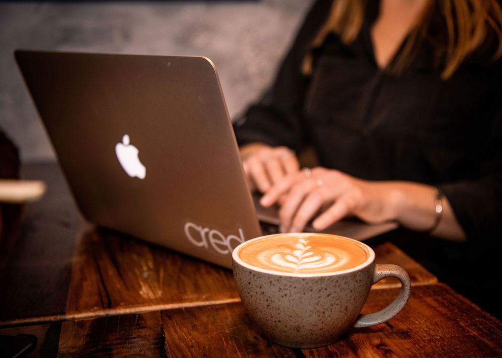 closeup of womans hands typing at lap top with pretty coffee sitting on table
