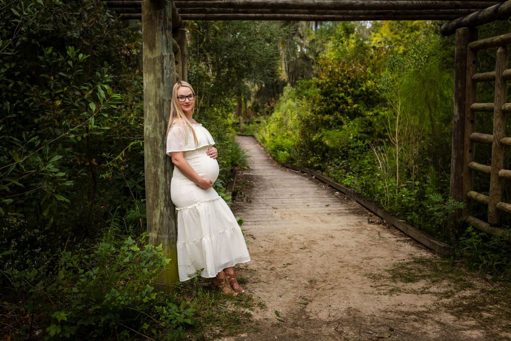 A dreamy maternity portrait on a rustic wooden path surrounded by lush greenery.