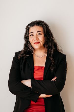 Studio portrait of person in black blazer and red dress against white background.