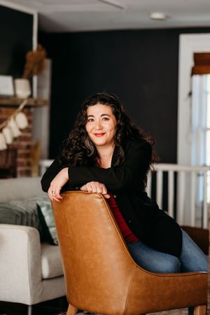 Portrait of person in black blazer sitting casually on brown leather chair.