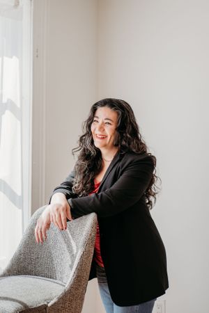 Candid portrait of person in black blazer laughing by window with natural light.