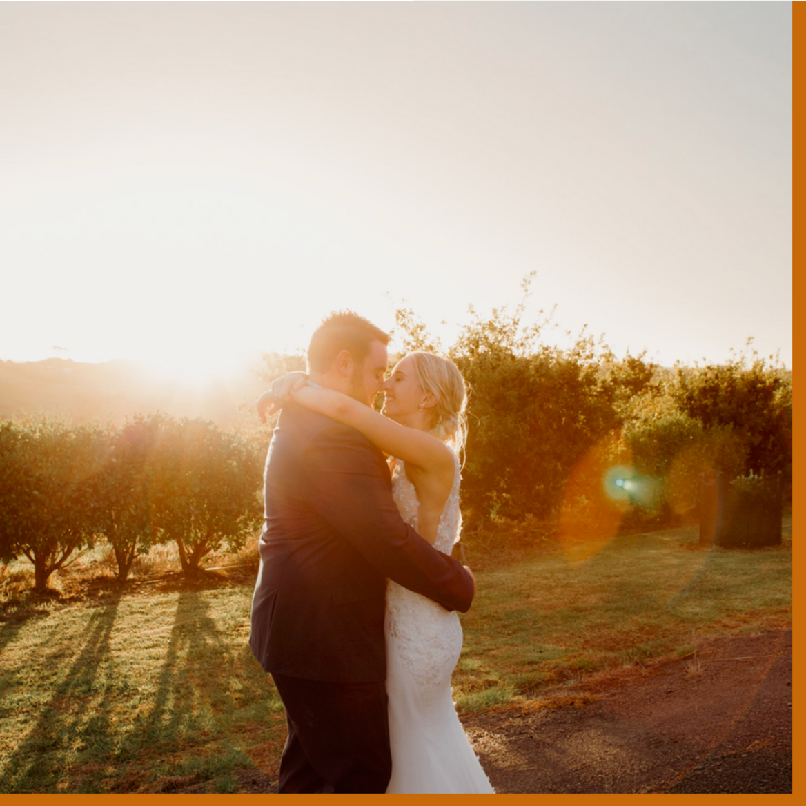 bride and groom touching foreheads while hugging at sunset in front of trees field
