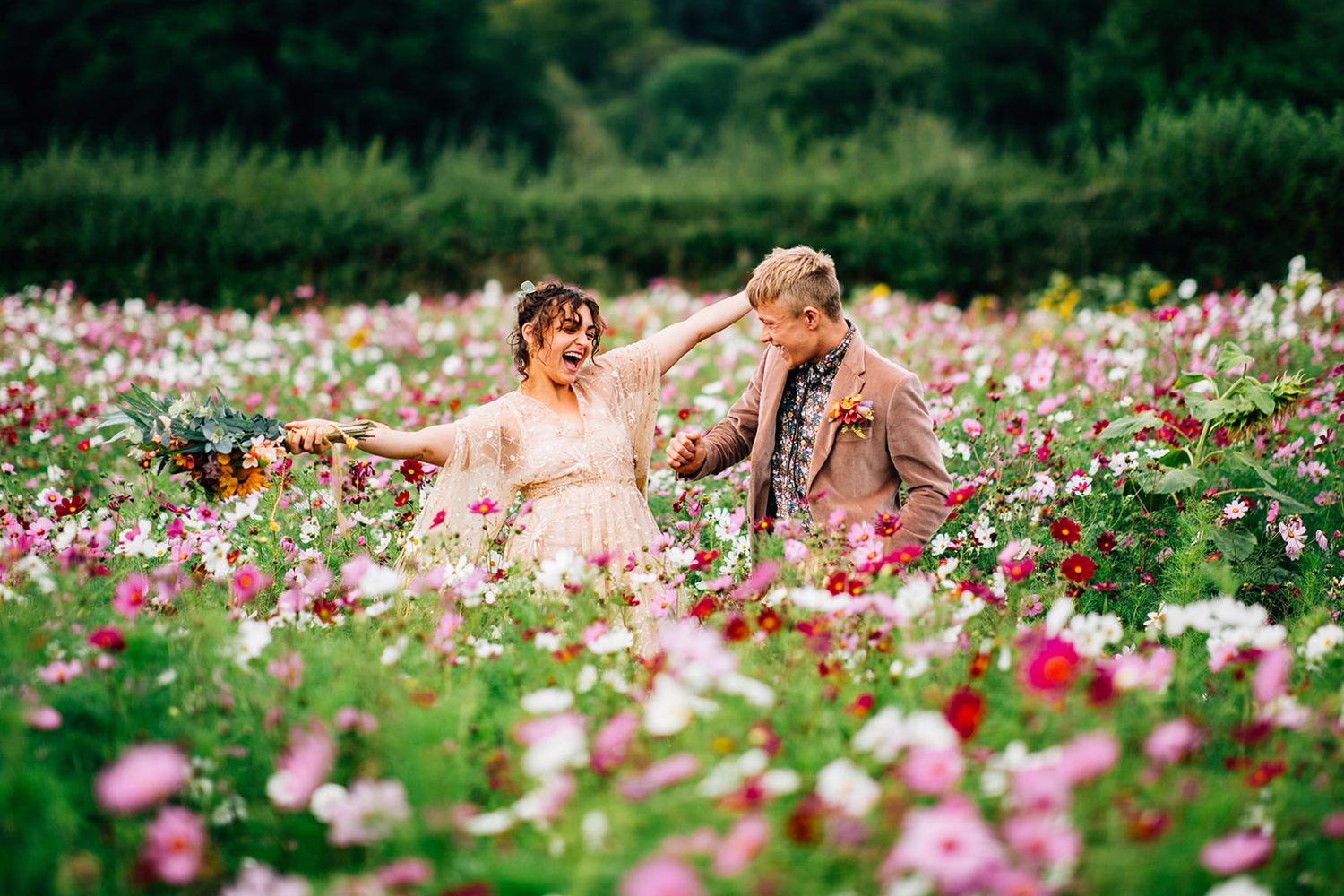 Couple embraces in field of pink cosmos flowers during sunset.