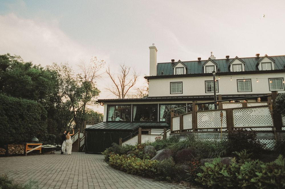 A large white house with dormers and a stone driveway at dusk.