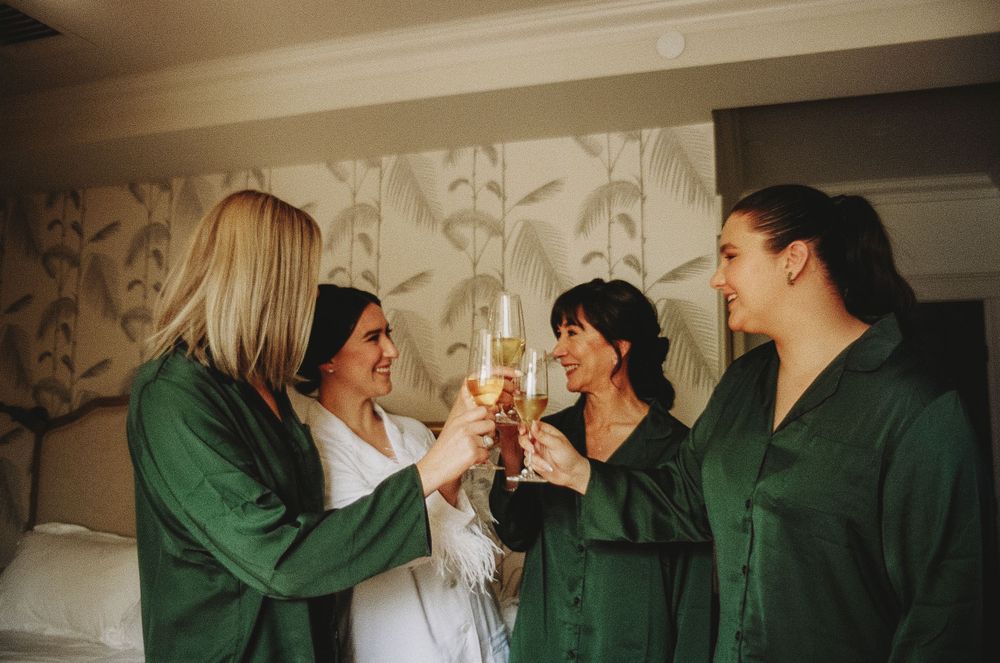 People in matching green robes toast with champagne glasses in a decorated room.