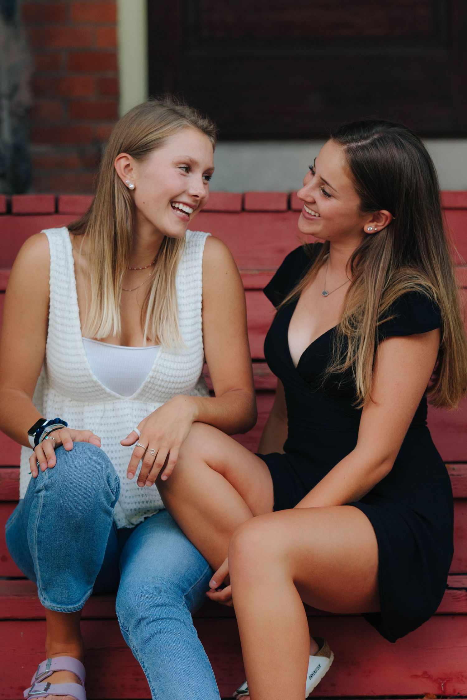 Two friends laughing and sitting together on red steps outdoors.