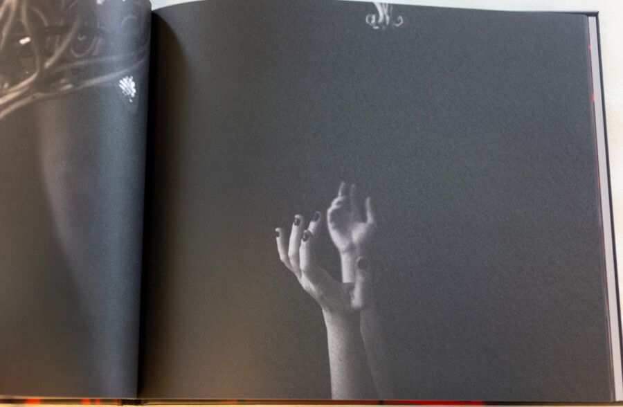 Monochromatic art book page featuring a ghostly image of outstretched hands against dark background.