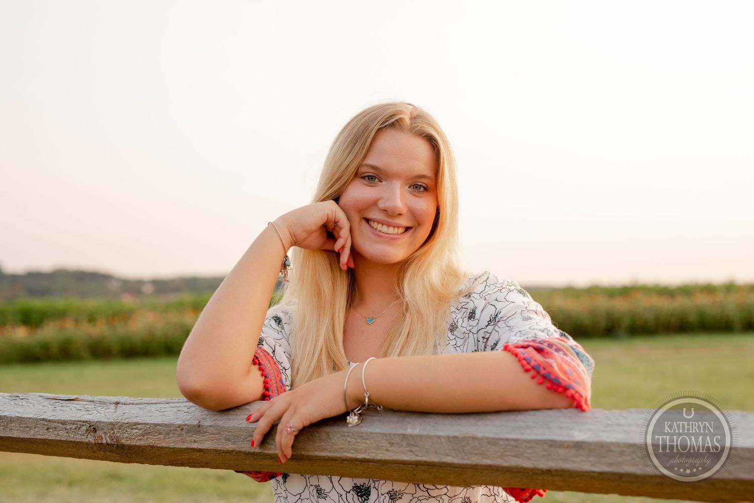 A woman rests against a wooden fence during golden hour in the countryside.