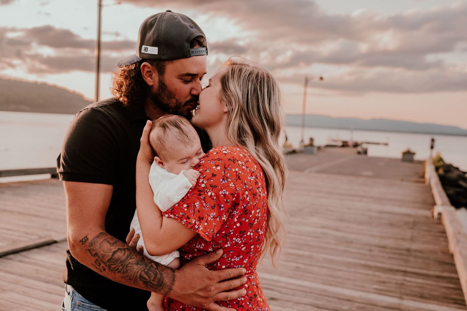 Intimate moment between couple with their baby on oceanside boardwalk during sunset.