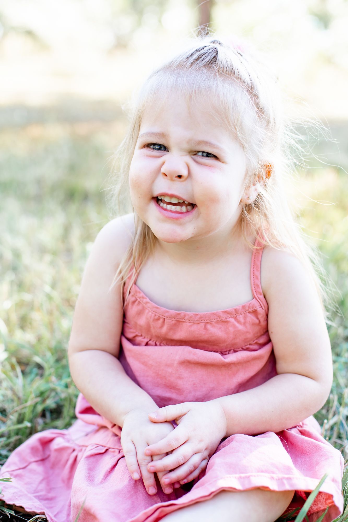 Toddler girl sits in the grass and smiles in Black Forest, Colorado.