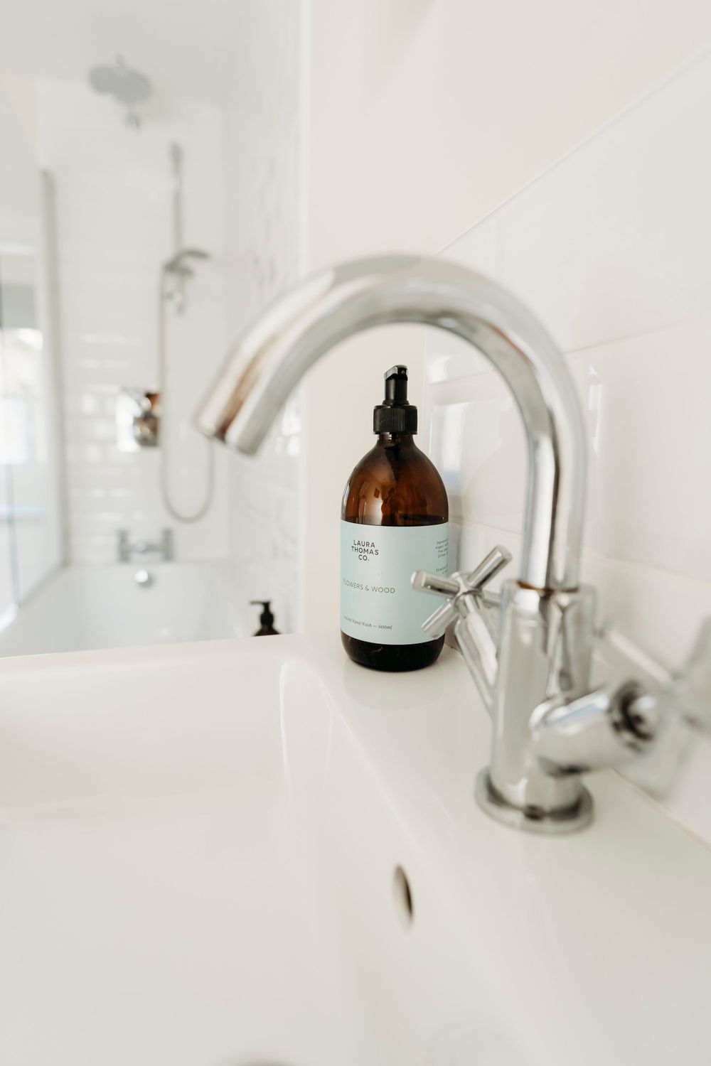 Modern chrome faucet and amber glass bottle in a white bathroom.