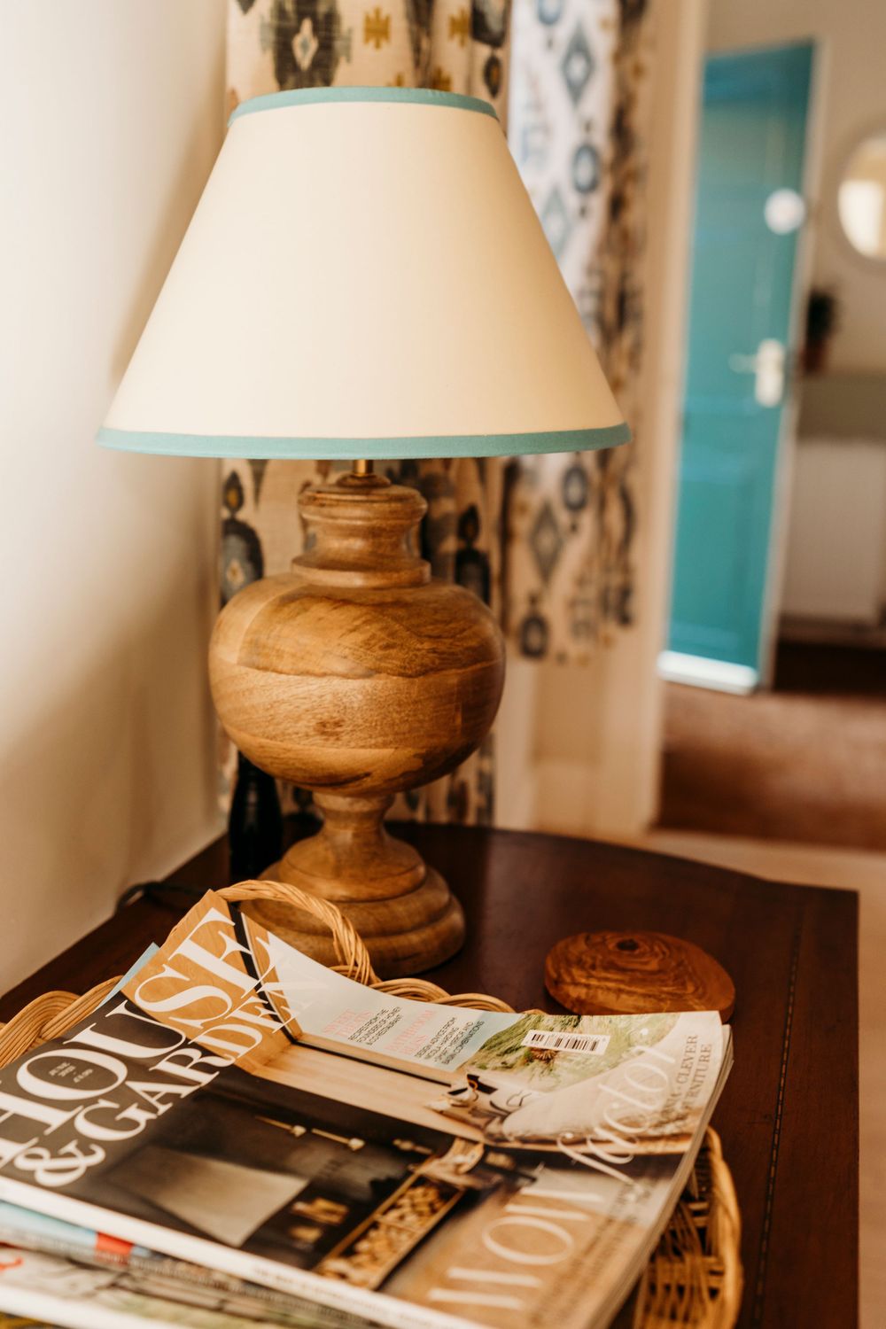Wooden table lamp with cream shade next to stack of magazines.