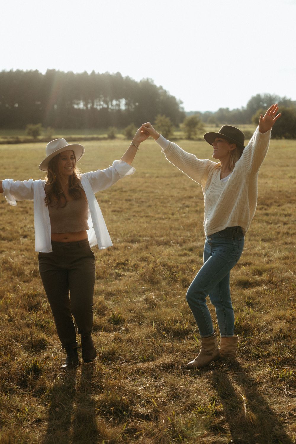 Silhouettes of two people dancing playfully in a sunlit field at dusk.