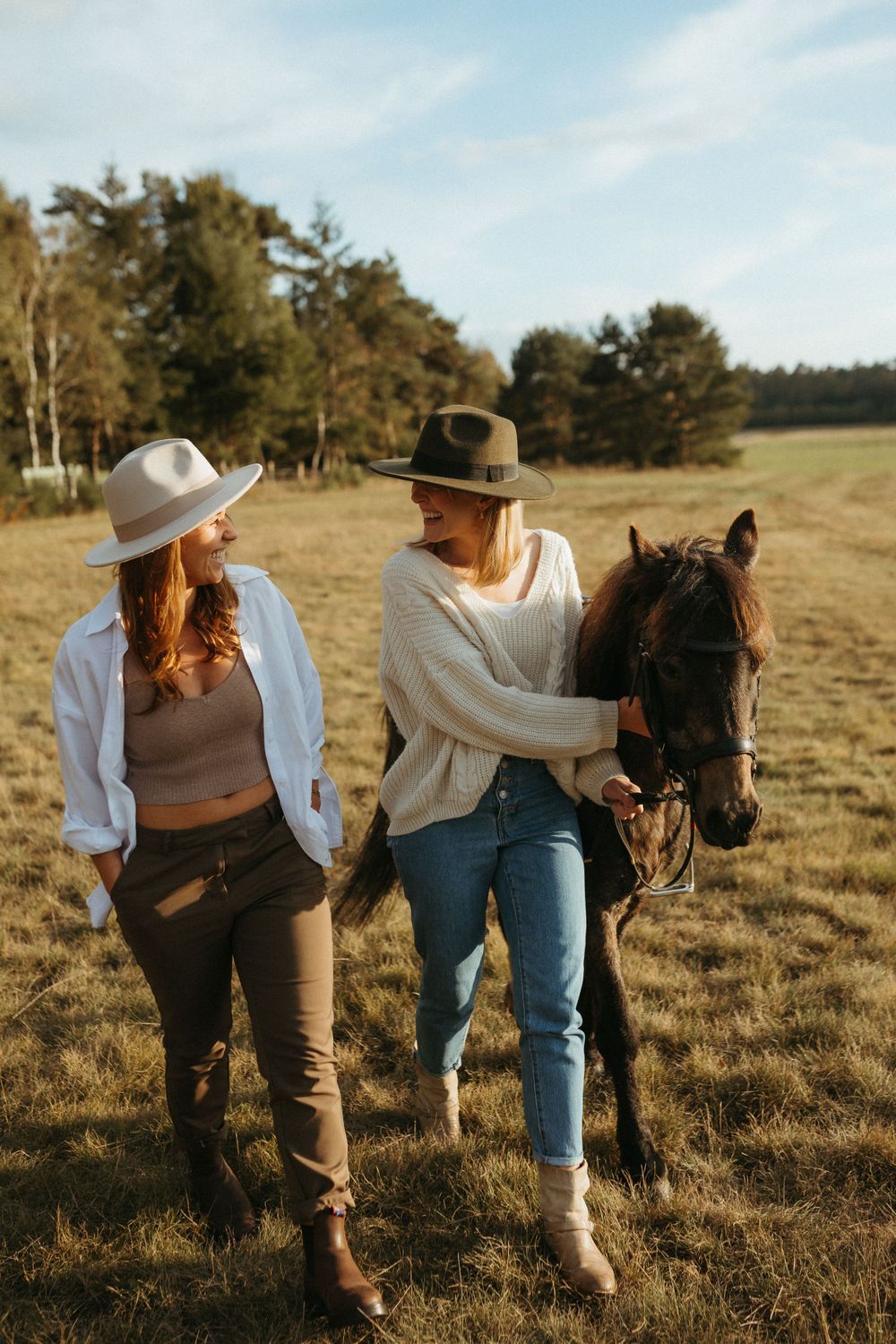 People in western wear interacting with a dark horse in a grassy meadow.