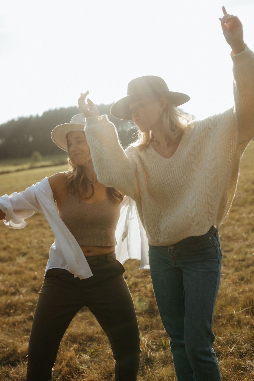 Friends dancing together in a field during golden hour wearing sweaters and hats.