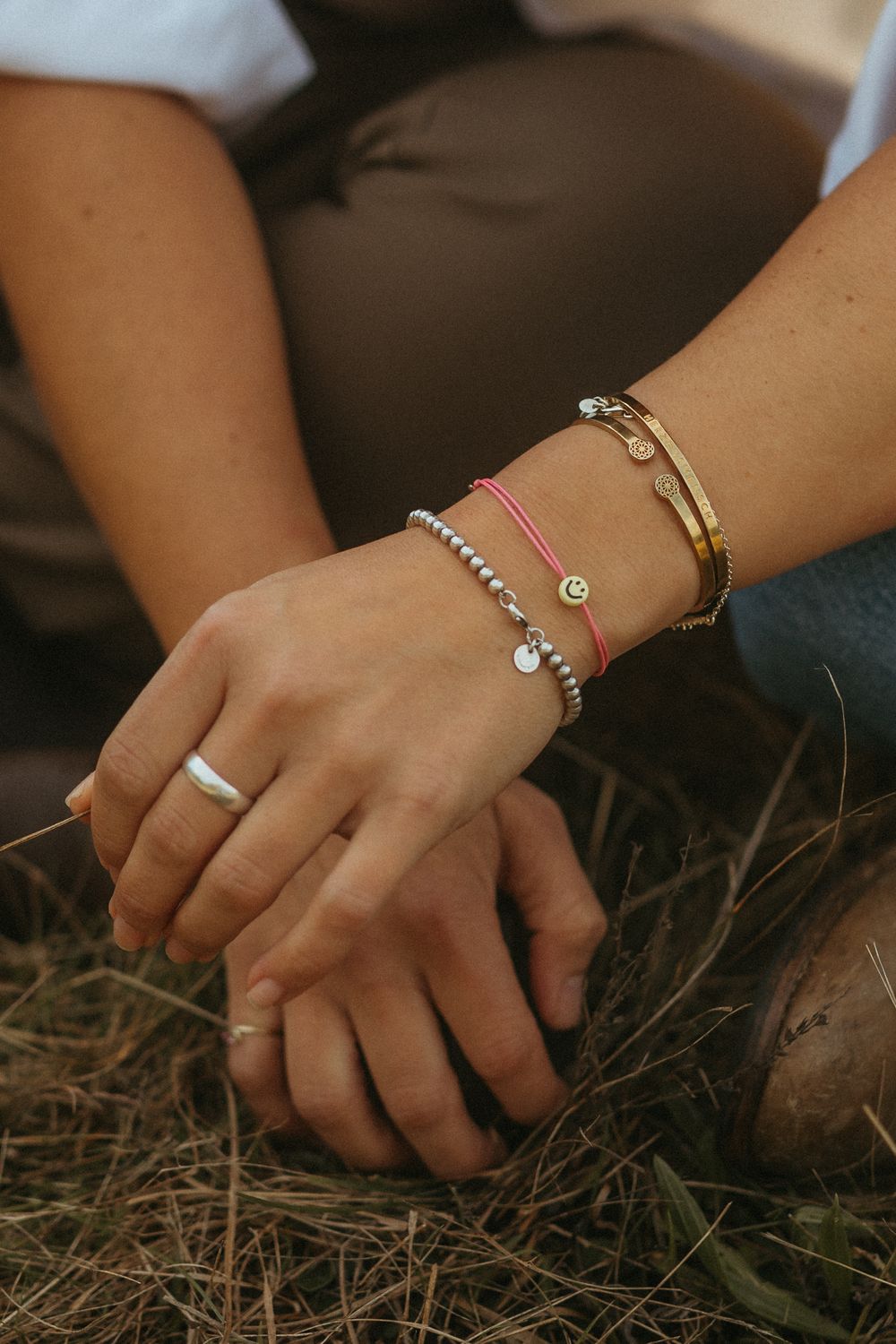 Close-up view of hands with delicate bracelets and jewelry against a natural hay background.