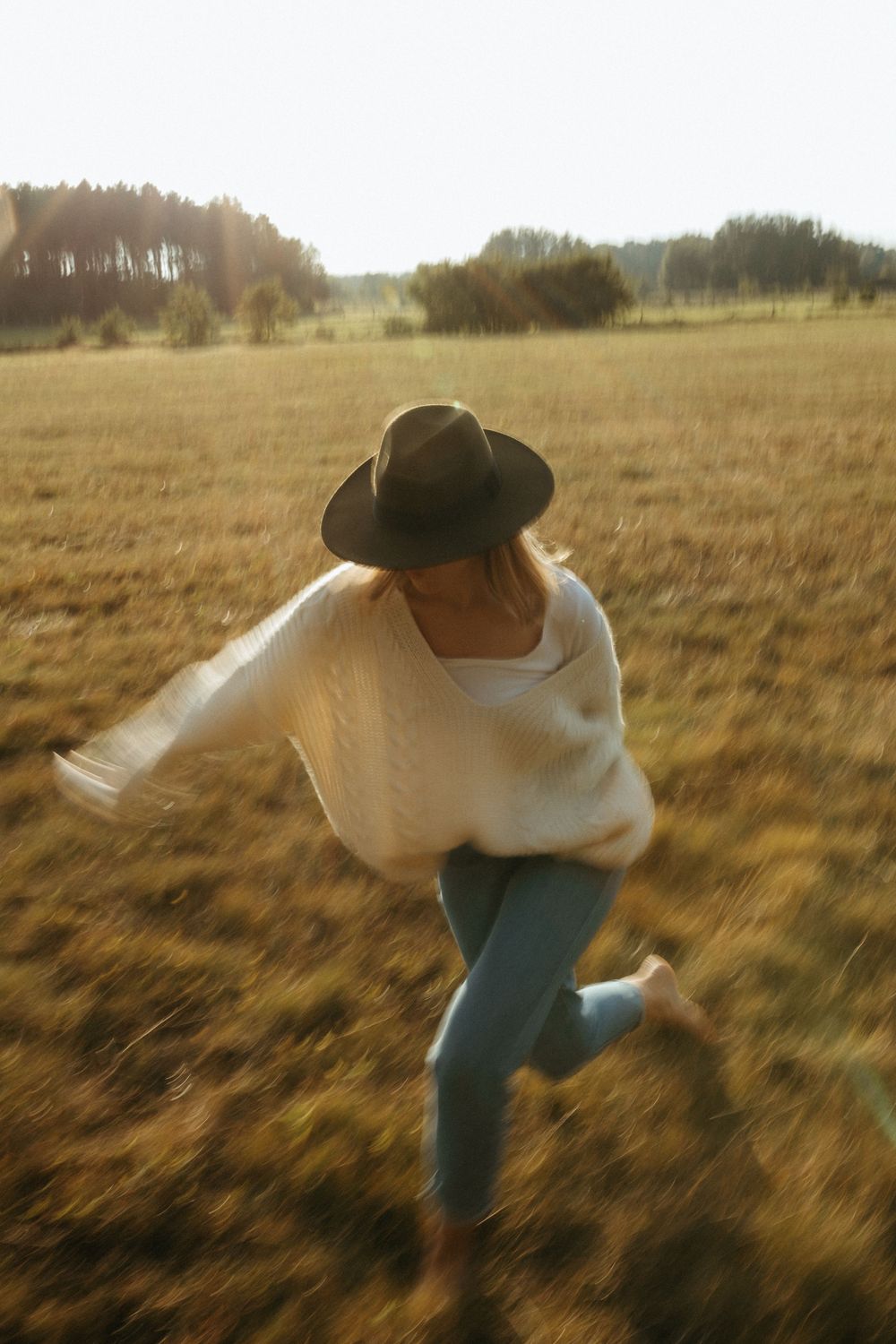 Person in white top and jeans dancing freely in a sun-drenched field at golden hour.