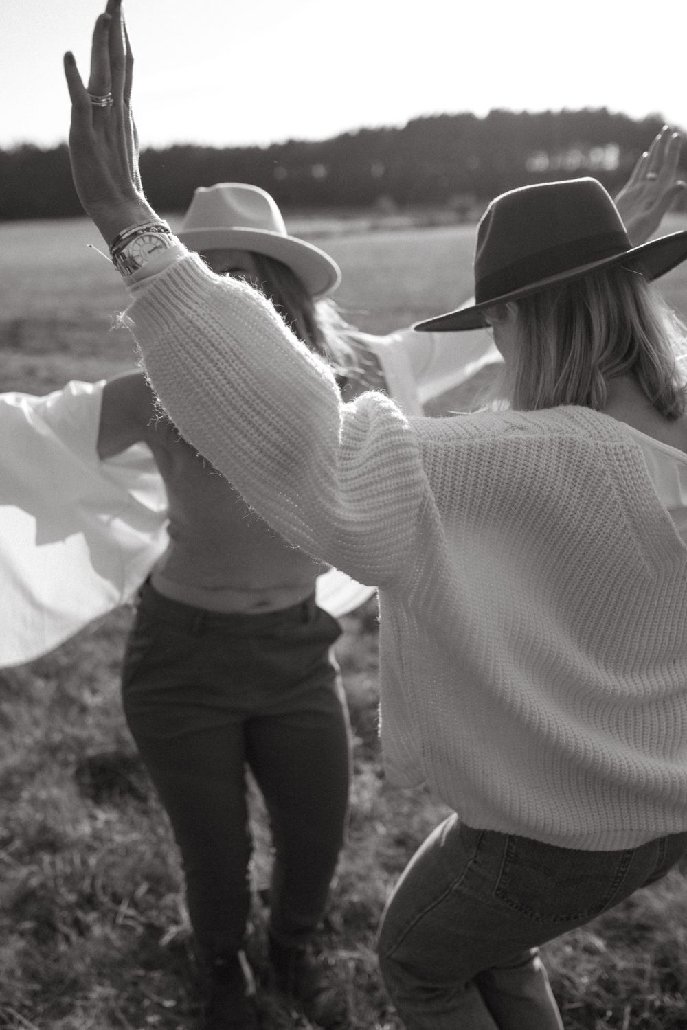 Black and white shot of friends enjoying a carefree moment outdoors with arms raised.