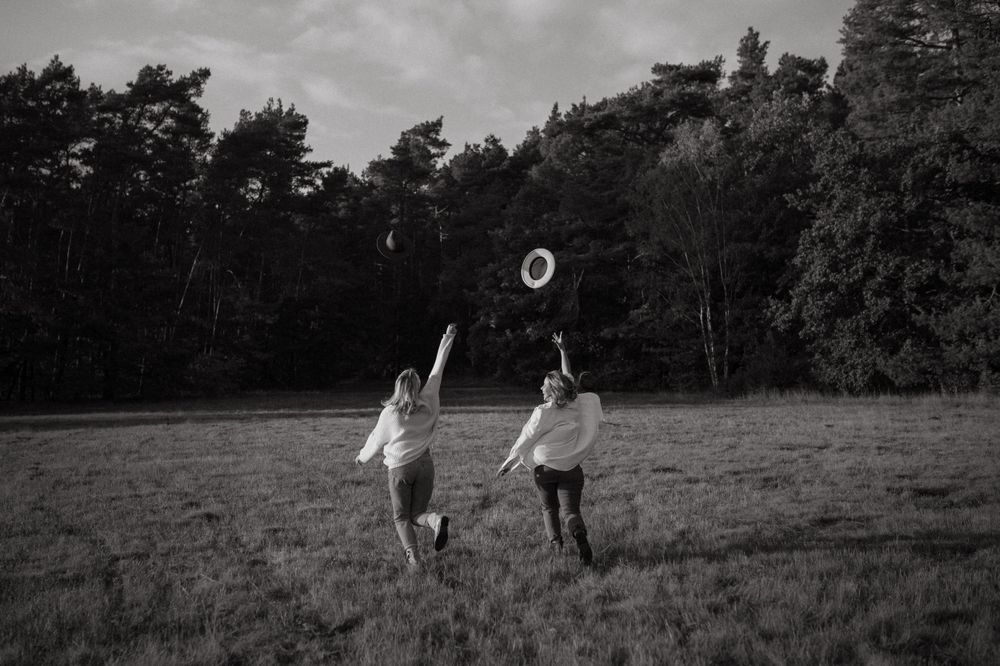 Friends playing in a meadow captured in black and white against a forest backdrop.