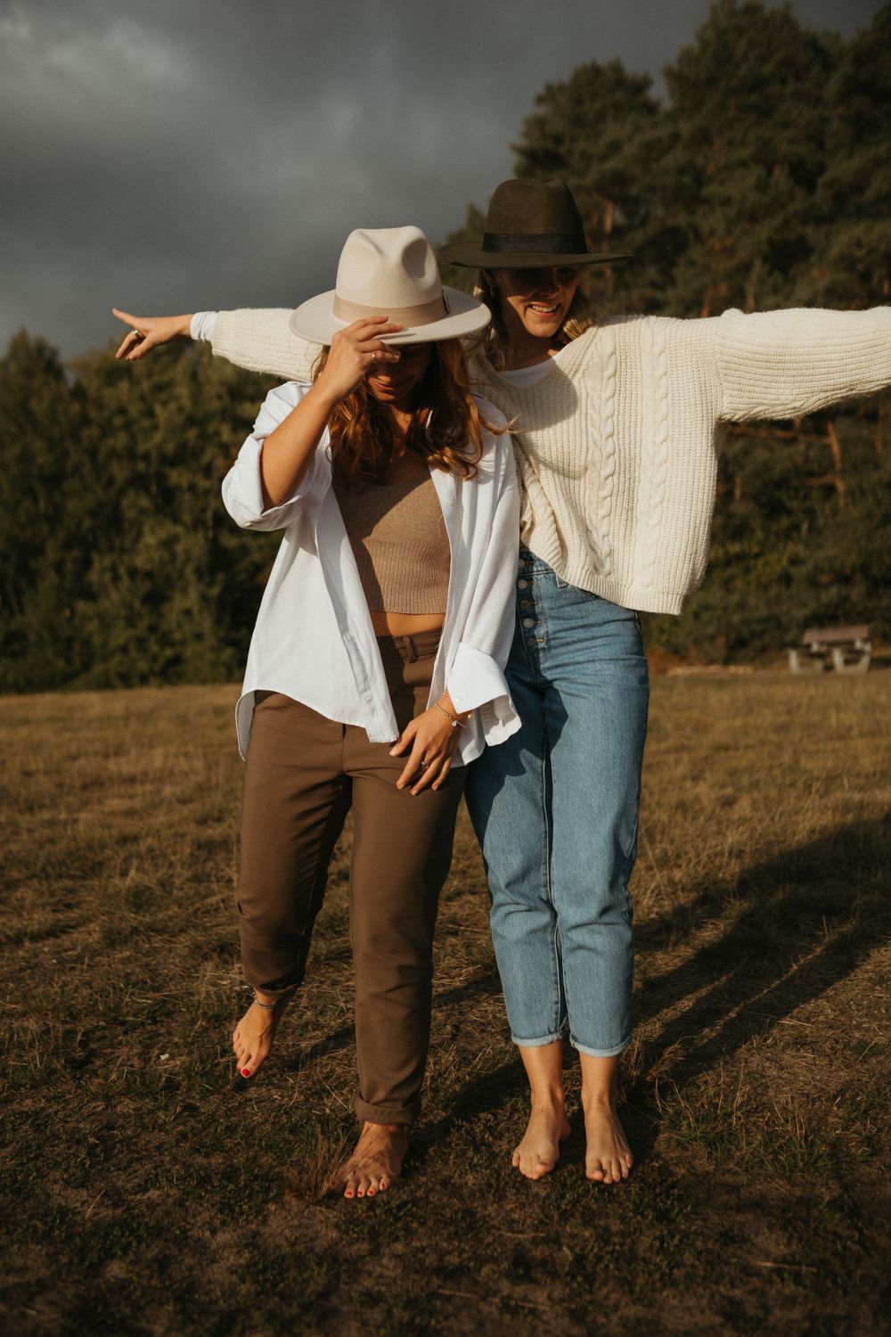 Two people in casual attire dancing playfully in a sunlit field at dusk.