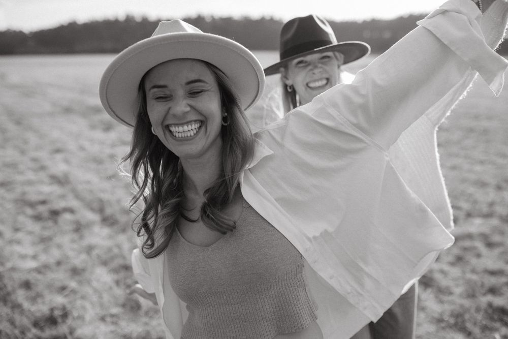 Candid shot of friends sharing authentic laughter in a sun-drenched field while wearing casual clothing.