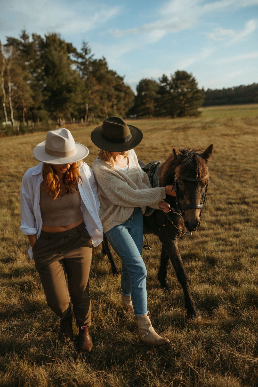 Two people in cowboy hats walking alongside a horse in a rustic field.