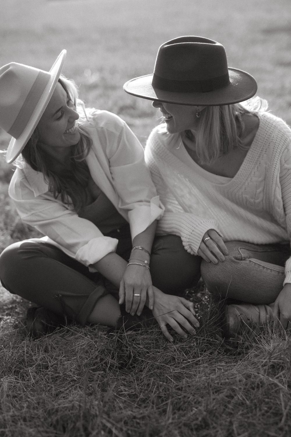 Two friends lying in the grass wearing hats and casual attire, captured in black and white.