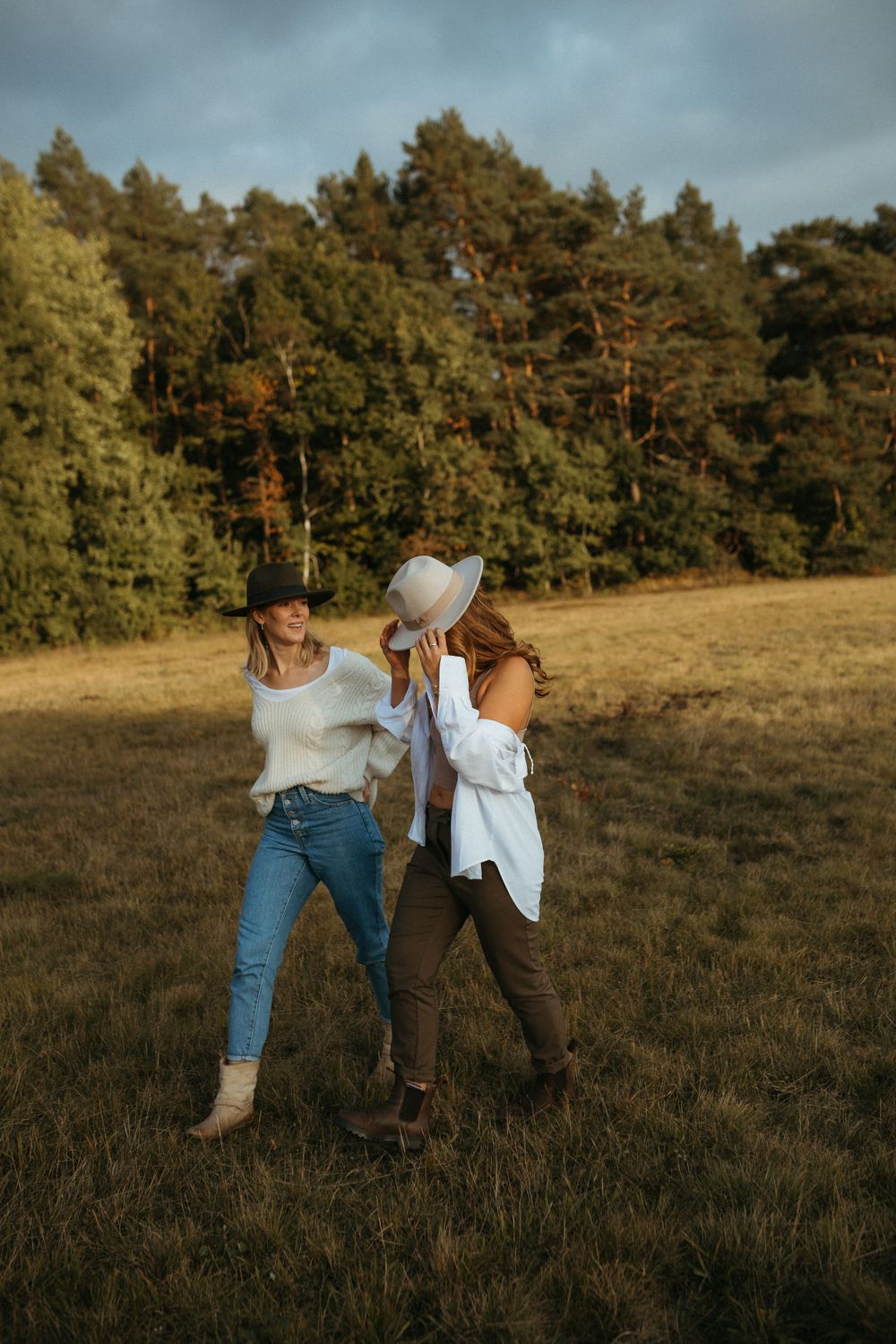 People in casual outfits dancing playfully in a golden field at sunset.
