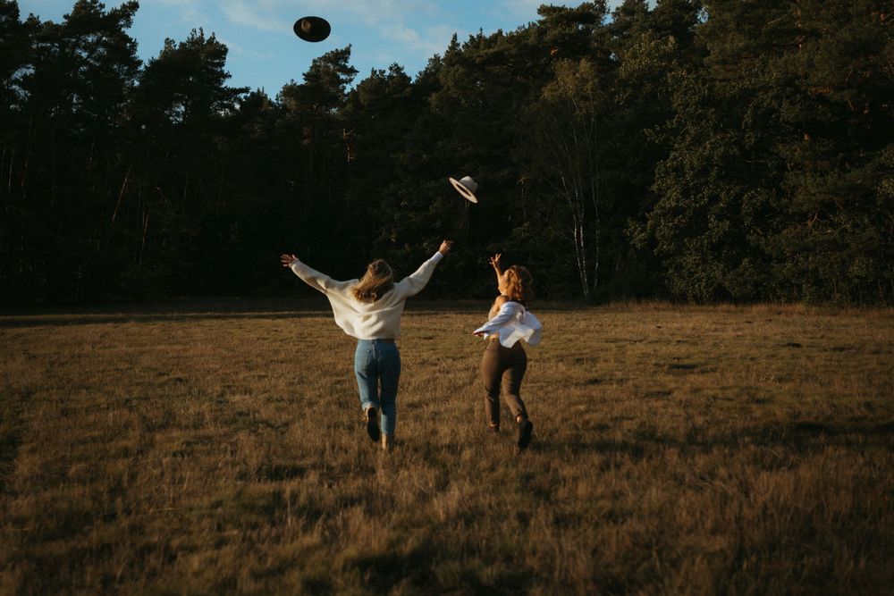 Two friends toss a football in a sunlit meadow bordered by tall trees.