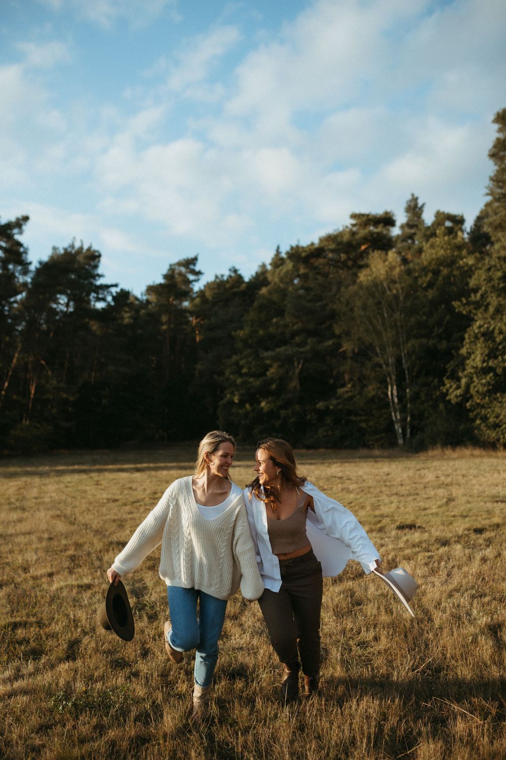 Friends laugh together in a golden field during sunset with pine trees in background.