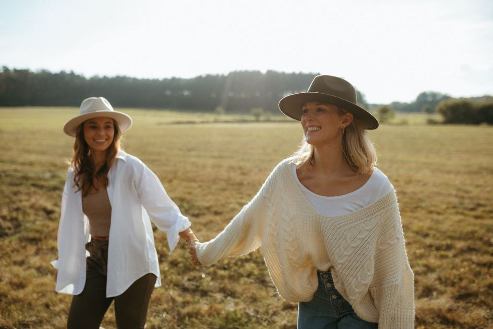 Friends in light colored sweaters enjoying a sunny day in an open field.