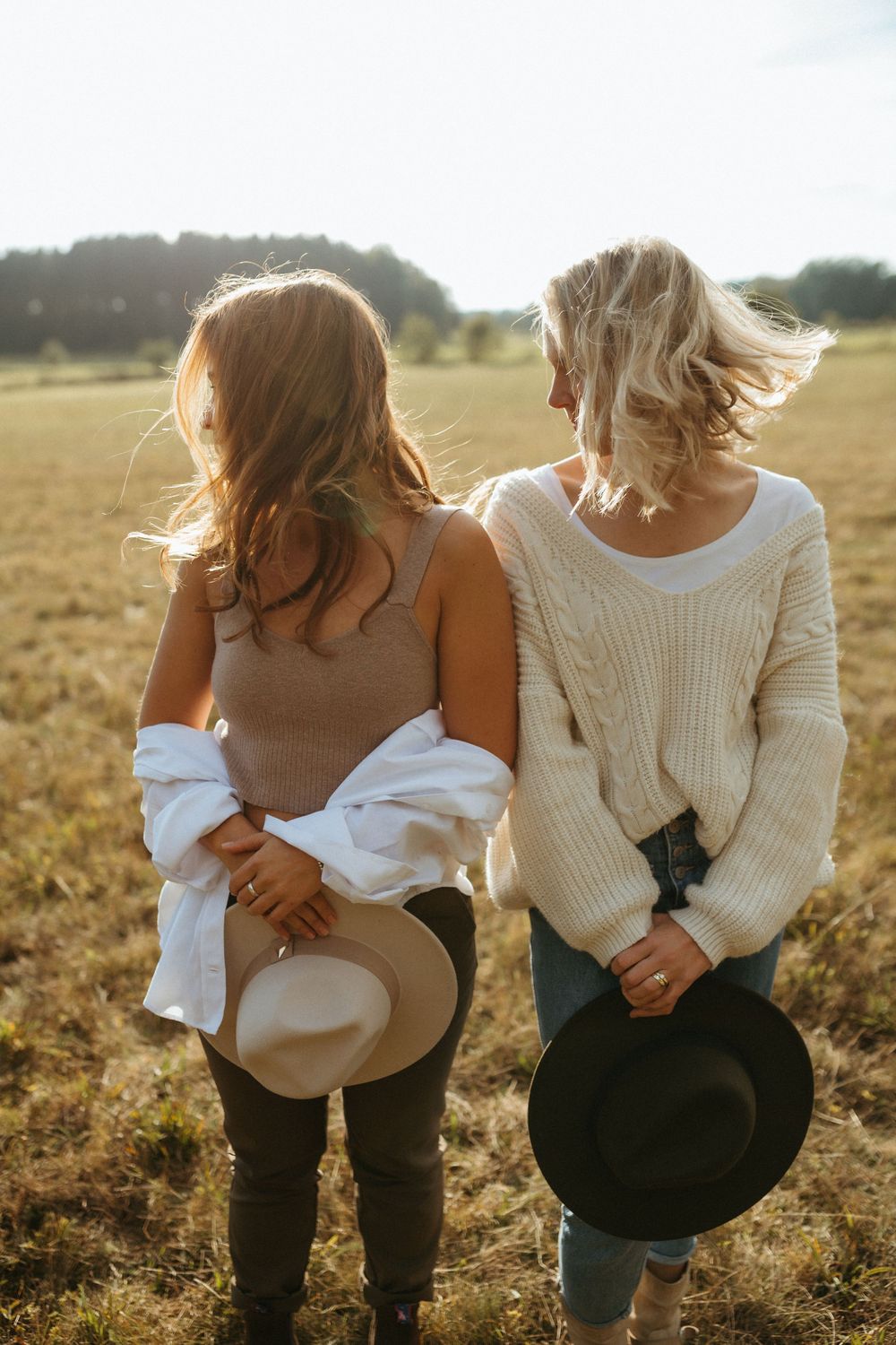 Back view of two people holding hats while enjoying a moment together in a sunny field.