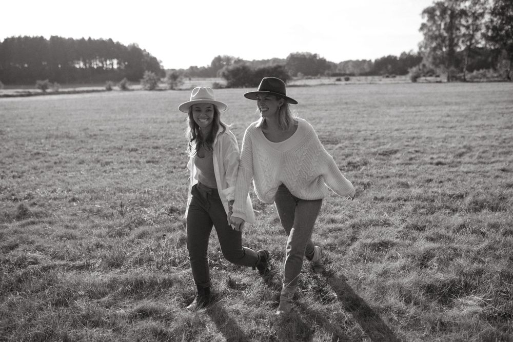 Black and white photo of two companions walking through an open field with trees in the distance.