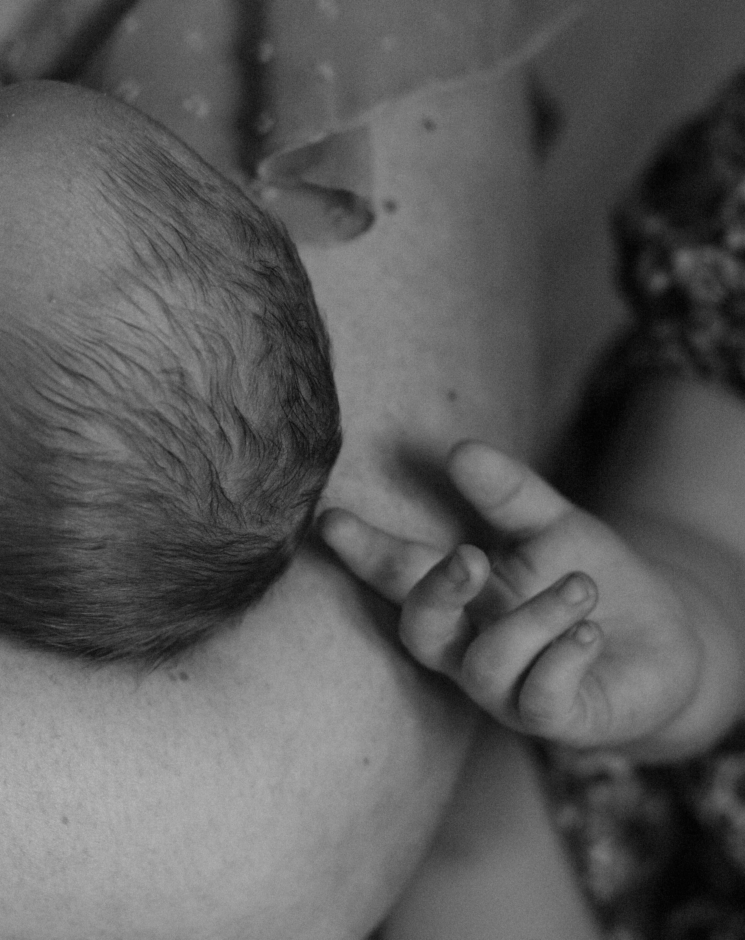 Black and white close-up of newborn baby nursing with tiny hand resting gently.
