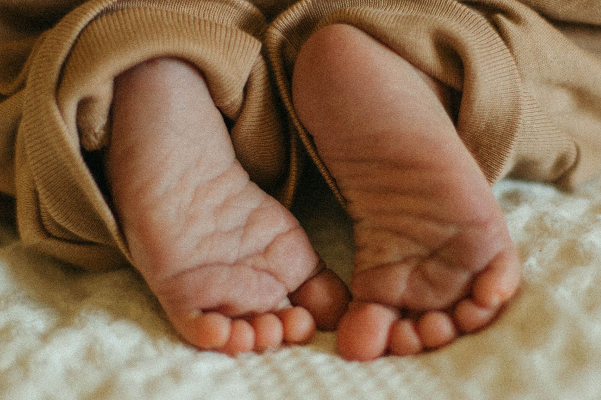 Close-up of tiny newborn baby feet peeking out from soft tan blanket.