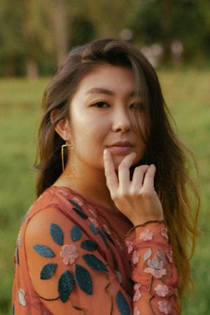 Young Asian woman in floral dress posing outdoors in a green park.