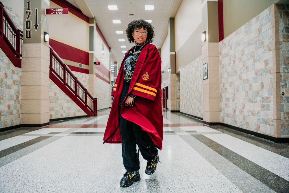 A stylish outfit featuring a red cape-style coat with colorful stripes worn in a school hallway.