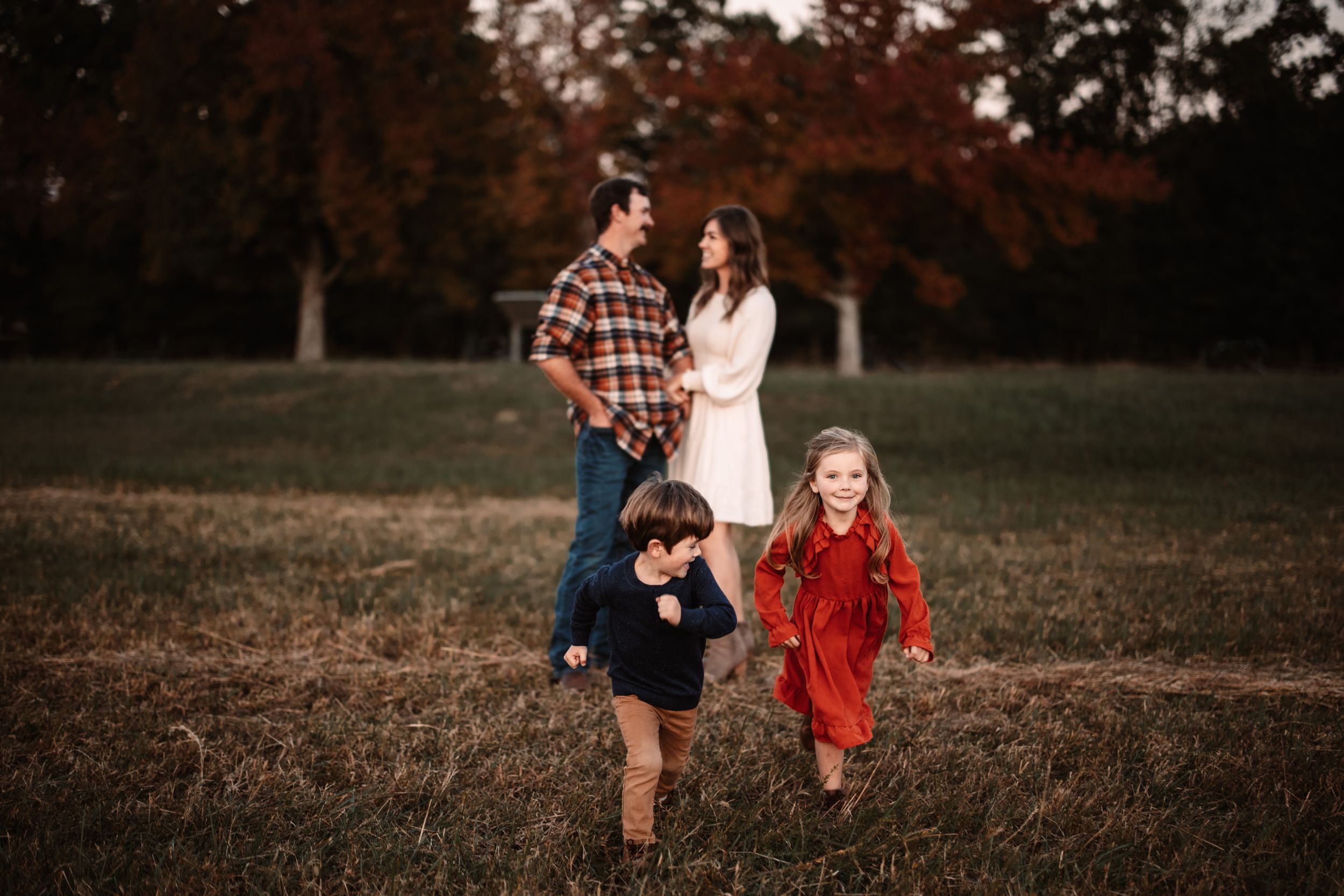 Children run playfully through field during autumn family photo session.