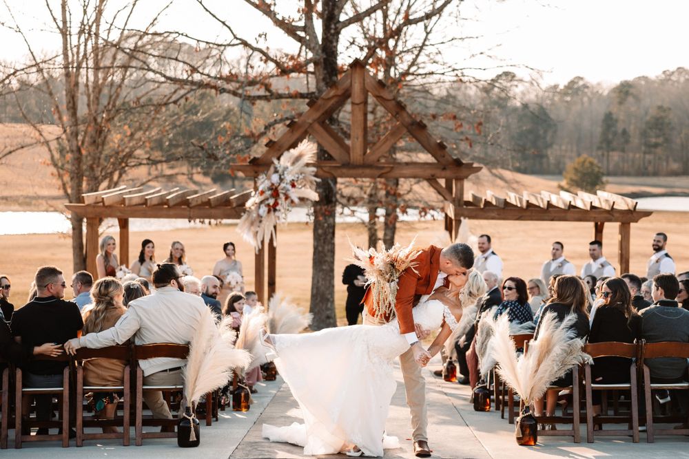 A joyful wedding celebration under a rustic wooden pavilion with guests seated on wooden chairs.