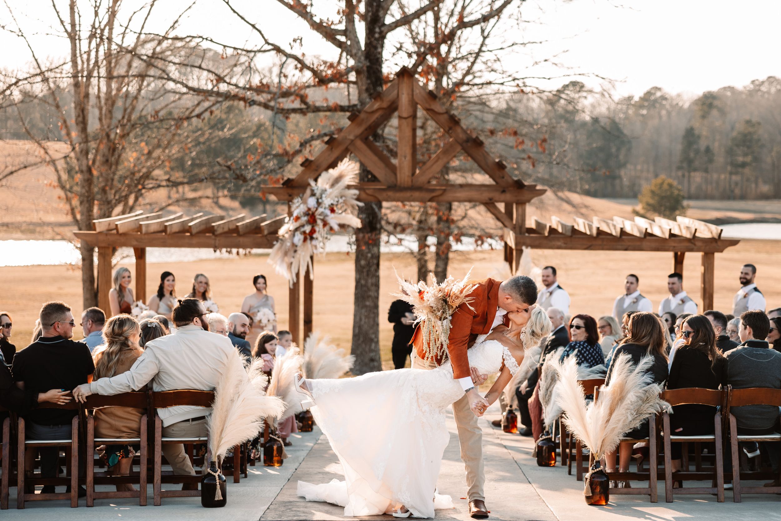 A joyful wedding celebration under a rustic wooden pavilion with guests seated on wooden chairs.